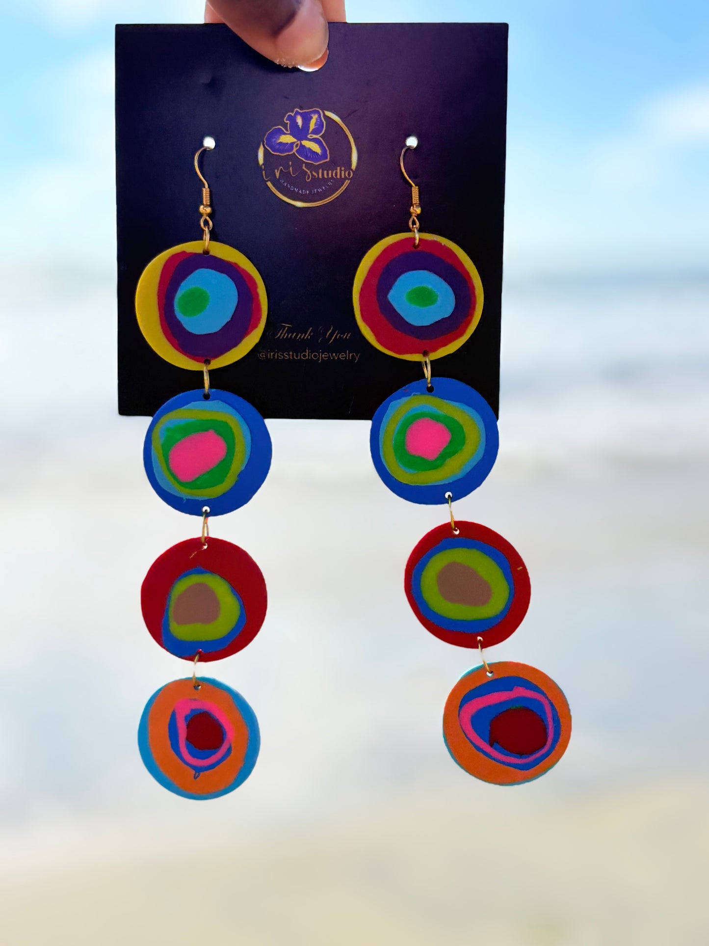 Colorful circular earrings on a branded card with a blurred background