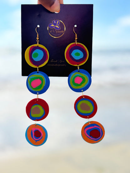 Colorful circular earrings on a branded card with a blurred background