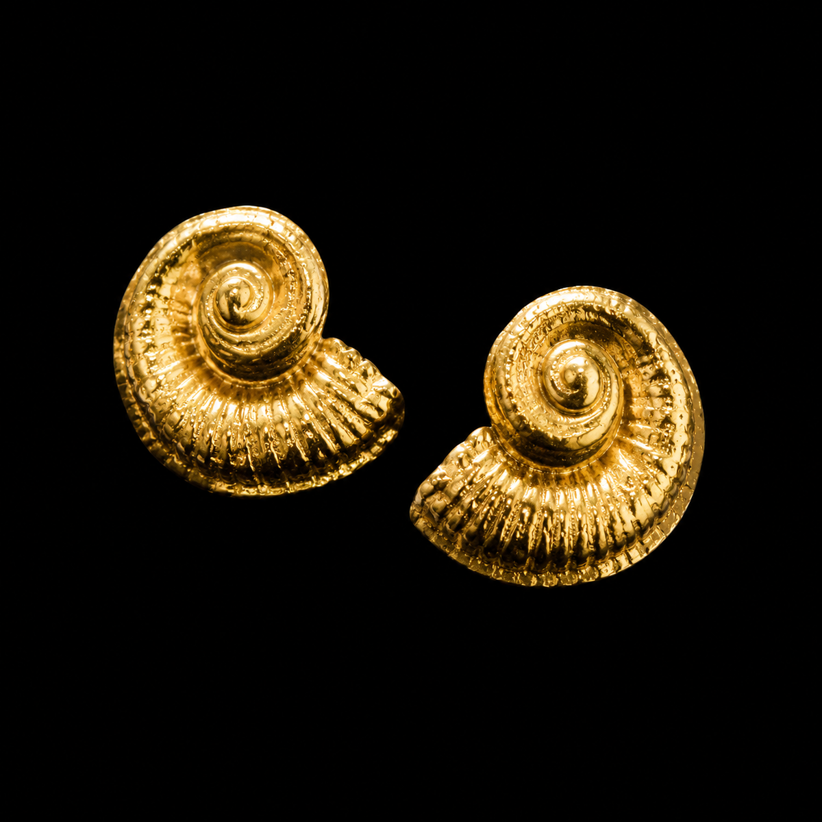 A pair of textured gold spiral stud earrings shaped like nautilus shells, shown on a solid black background.
