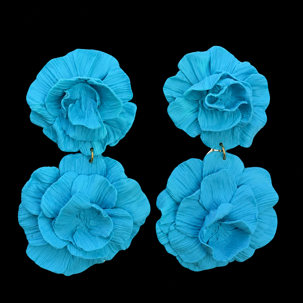 A pair of large, vibrant turquoise blue flower-shaped earrings with textured, pleated petals and small gold-tone posts, displayed against a solid black background.