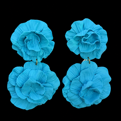 A pair of large, vibrant turquoise blue flower-shaped earrings with textured, pleated petals and small gold-tone posts, displayed against a solid black background.